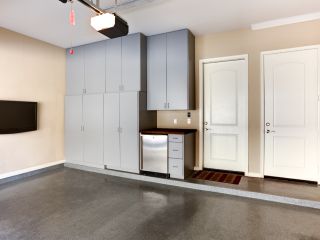 Custom Garage Storage Cabinets and Organization in Blaine MN Modern garage interior with sleek gray storage cabinets, wall-mounted TV, mini fridge, and two white entry doors in Blaine, Minnesota.