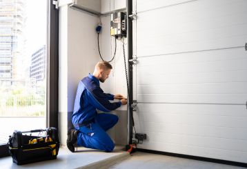 Garage door technician in blue uniform repairing a modern garage door system with tools inside a Blaine, Minnesota garage.