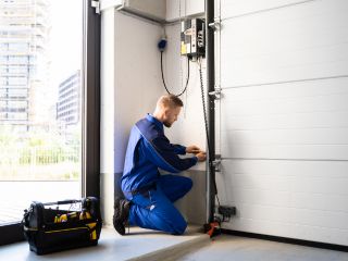 Technician Performing Garage Door Repair in Blaine MN Garage door technician in blue uniform repairing a modern garage door system with tools inside a Blaine, Minnesota garage.