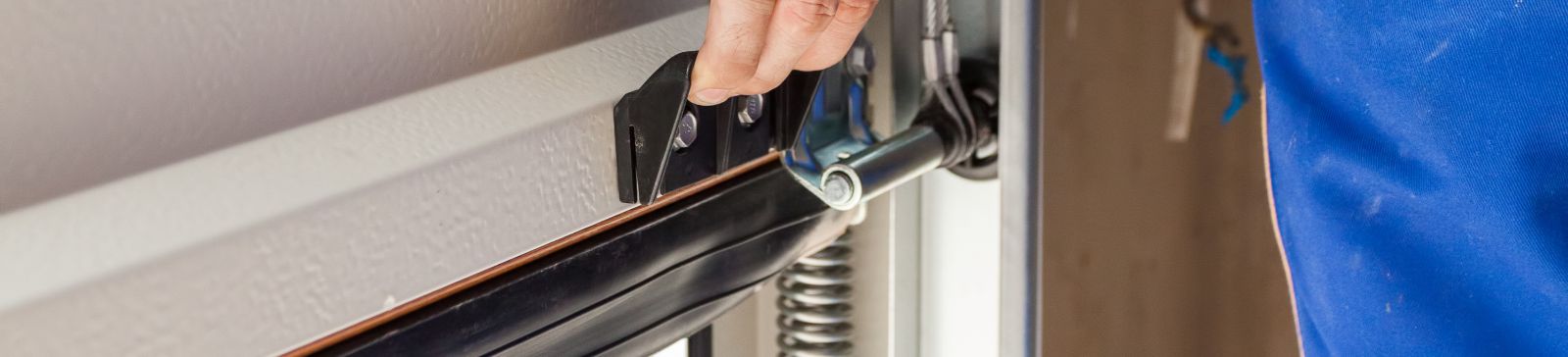 Close-up of a technician in blue uniform adjusting a garage door bracket and spring in Blaine, Minnesota.