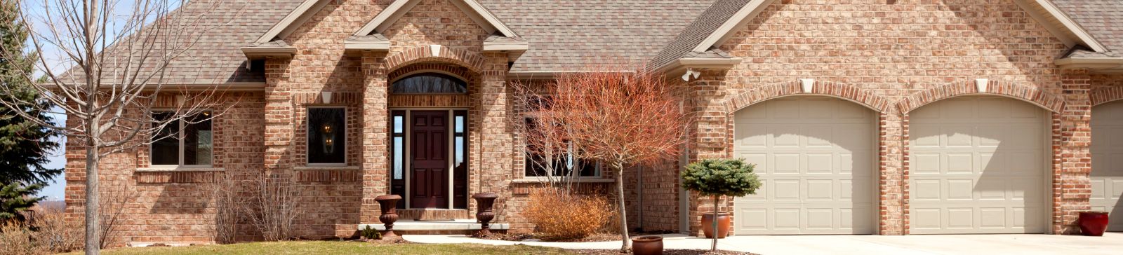 Front view of a brick house with two beige garage doors and a landscaped yard in Blaine, Minnesota.