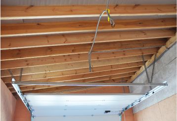 Garage ceiling with visible wooden beams, a newly installed garage door rail, and spring assembly in Blaine, Minnesota.