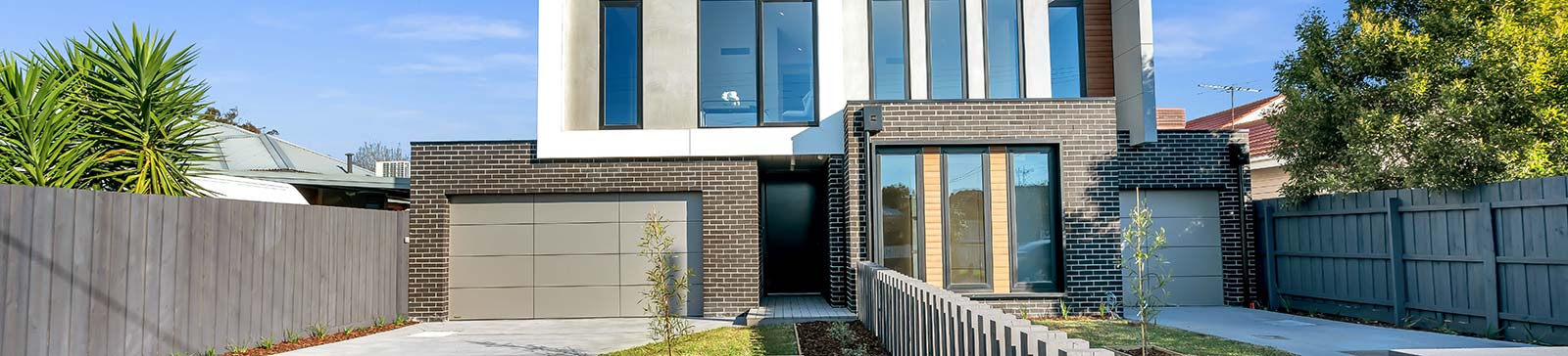 Contemporary two-story house with two beige garage doors, brick facade, and landscaped front yard in Blaine, Minnesota.