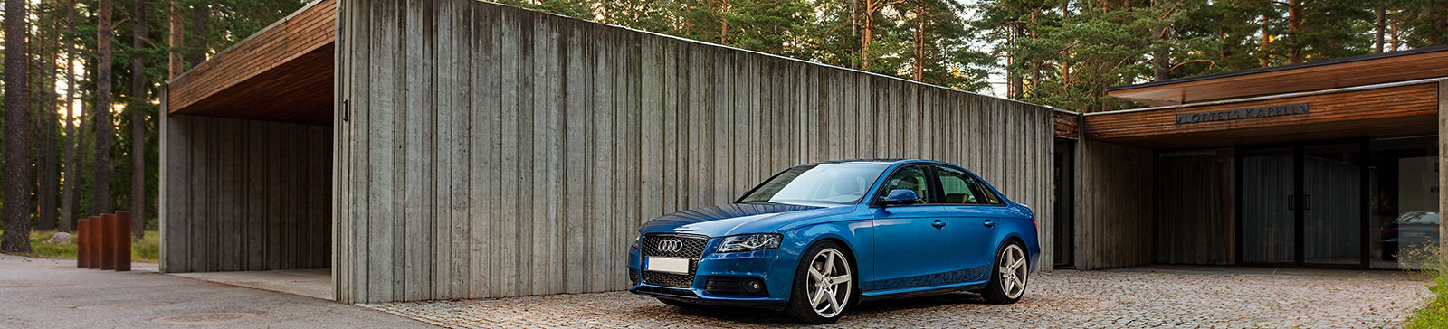 Sleek blue car parked in front of a modern, minimalist garage surrounded by trees in Blaine, Minnesota.