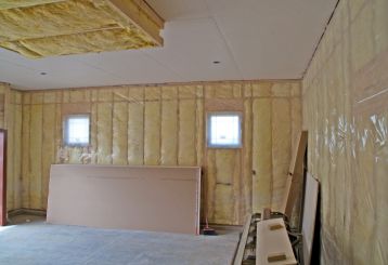 Garage interior with new insulation, drywall sheets, and plastic vapor barrier installed on walls and ceiling in Blaine, Minnesota.